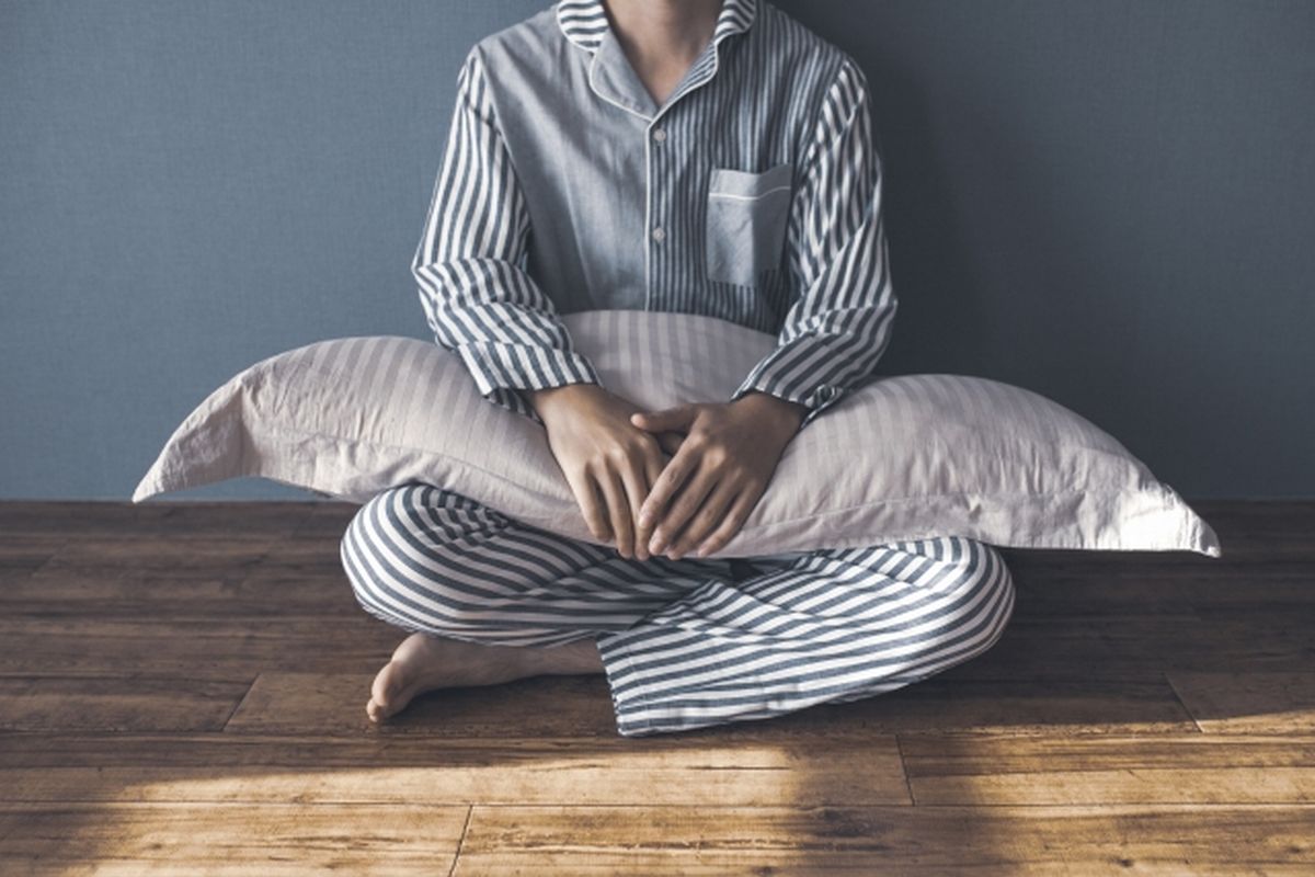 パジャマ姿で枕を抱え、座り込んでいる男性の画像。昼寝や強い眠気（傾眠傾向）を象徴するイメージ。