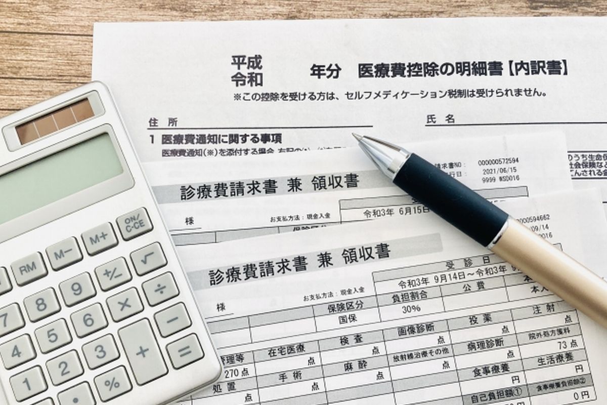 医療費控除の明細書と医療費の領収書、その上に置かれた電卓とペンの明るい雰囲気の写真