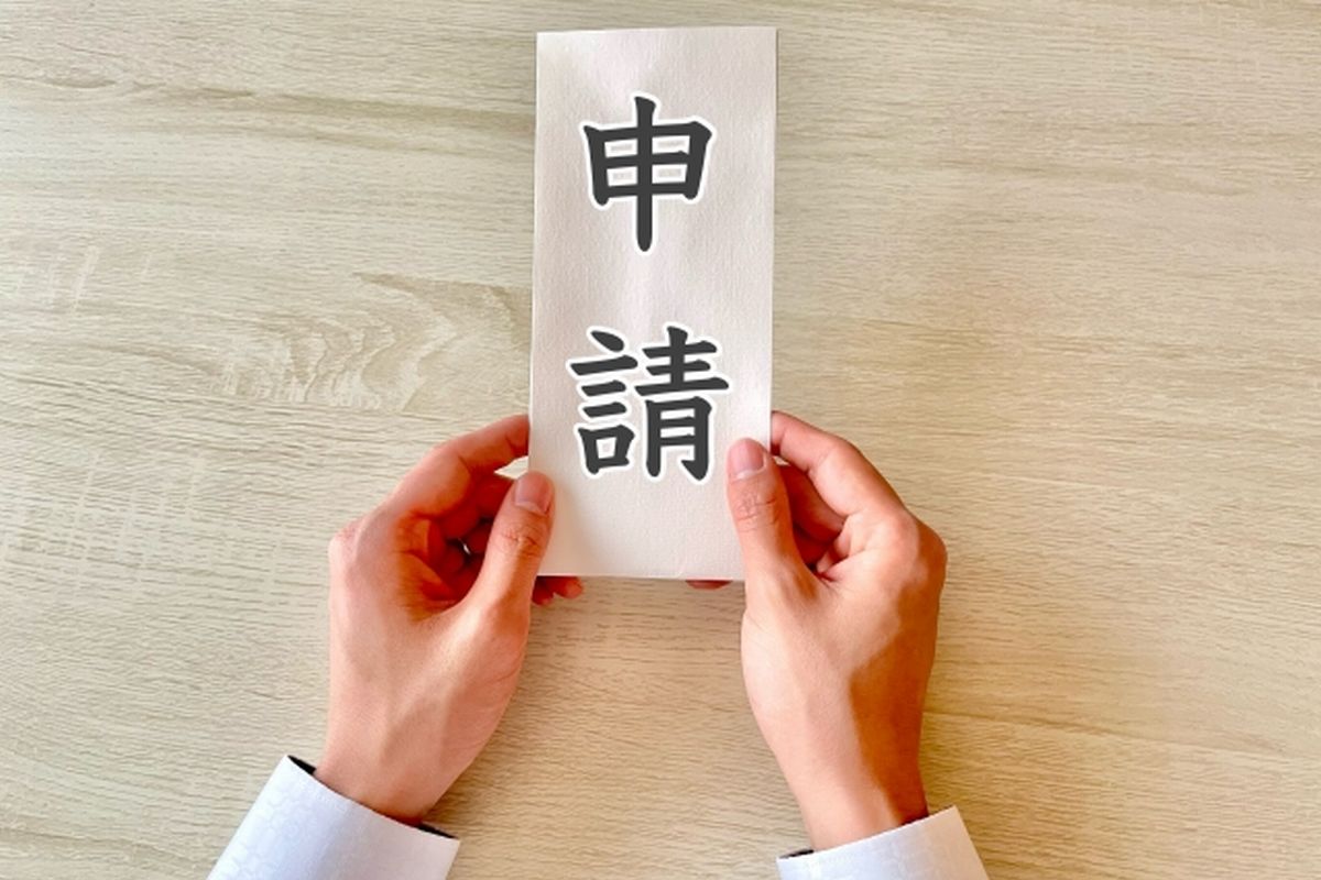 机上で「申請」と書かれた紙を両手で差し出す様子