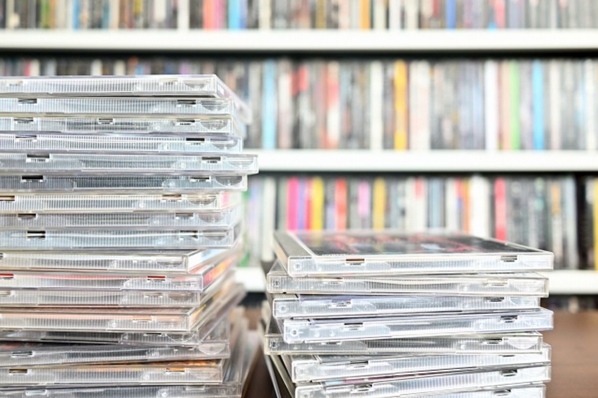 CDが棚に並び、手前にケースが平積みされた雑多な部屋のイメージ